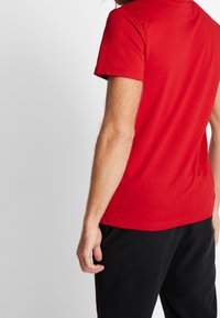 Camiseta roja de manga corta hecha de algodón, con un cuello redondo y una textura suave, combinada con pantalones de chándal negros.