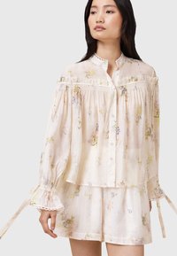 Lightweight, pale floral blouse with ruffled collar, buttons, and billowy sleeves, featuring delicate lace trim and soft, flowing fabric.