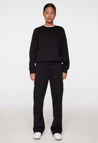 Sweatshirt noir et pantalon de jogging assorti en tissu doux. Le sweatshirt a un col rond et le pantalon a une taille élastique avec cordon de serrage. Baskets blanches.