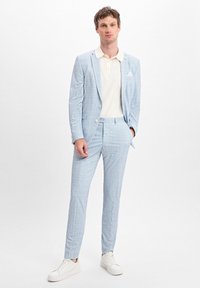 Hellblau kariertes Anzug mit tailliertem Schnitt, ergänzt durch ein cremefarbenes Polohemd und weiße Sneaker. Enthält ein dekoratives Einstecktuch.