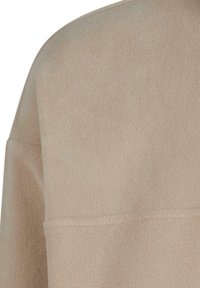 Beige fleece topp med myk tekstur, som har høy hals og en avslappet passform. Sømdetaljer gir subtil interesse til designet.