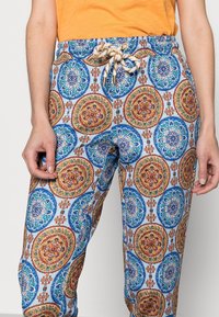 Lätta, mönstrade byxor med en blå bakgrund, som har intrikata cirkulära mönster i röd, orange och grön. Justerbart snörliv.