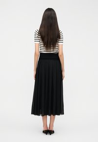 Μαύρη, αέρινη midi φούστα με εφαρμοστή μέση, σε συνδυασμό με ριγέ, κοντομάνικη μπλούζα, απεικονίζεται από πίσω σε απλό φόντο.