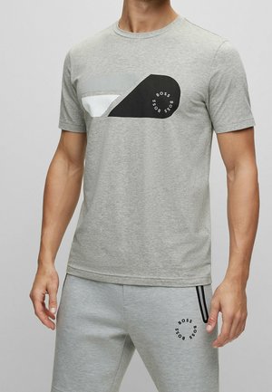 Mann trägt hellgraues T-Shirt und passende Sweatpants mit schwarz-weißem Grafik- und kreisförmigem "BOSS"-Schriftzug auf beiden Kleidungsstücken.