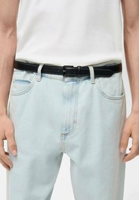 Zwarte leren riem met een rechthoekige gesp, gedragen over lichtblauwe denim jeans. De riem heeft een gladde textuur en meerdere verstelgaten.