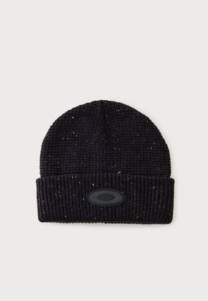 Gorro de punto acanalado negro con ala doblada y pequeña parche decorativo ovalado en la parte frontal.