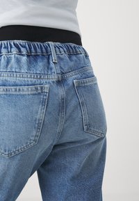 Light blue denim jeans with an elastic waistband, featuring two back pockets and a relaxed fit. Texture appears slightly worn and soft.