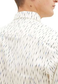 Chemise blanche avec un motif de lignes noires et bleues, dotée d'un col classique et d'un dos boutonné, fabriquée en tissu lisse.