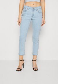 Light blue denim jeans with a slim fit, cropped length, and rolled cuffs. Features front pockets and a button closure. Paired with black strappy heels.