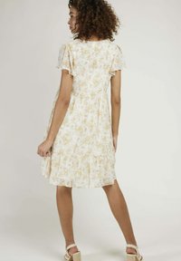 Robe florale avec une base crémeuse claire ornée de fleurs jaunes, des manches courtes bouffantes, une taille ajustée et un ourlet en volants superposés.