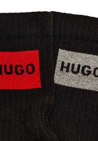 Calcetines negros con un parche rojo con "HUGO" en negro y un parche gris con "HUGO" en negro, textura de punto, longitud estándar.