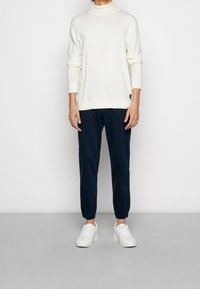 Vit stickad polotröja, marinblå tapered byxor och vita sneakers. Slät textur och enkelt mönster. Inga synliga mönster eller detaljer.