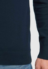 Pull en maille bleu marine avec des poignets et un ourlet côtelés. Texture lisse, design ajusté et fentes latérales pour un confort accru.