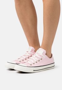 Rosa canvas-sneakers med vita sulor, svart rand och silverfärgade ögla. Har logotyppatch på tungan och klassisk tådeldesign.