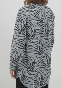 Camisa de patrón a rayas negras y grises, con mangas largas, corte entallado y dobladillo trasero más largo. Presenta una suave textura en la tela.