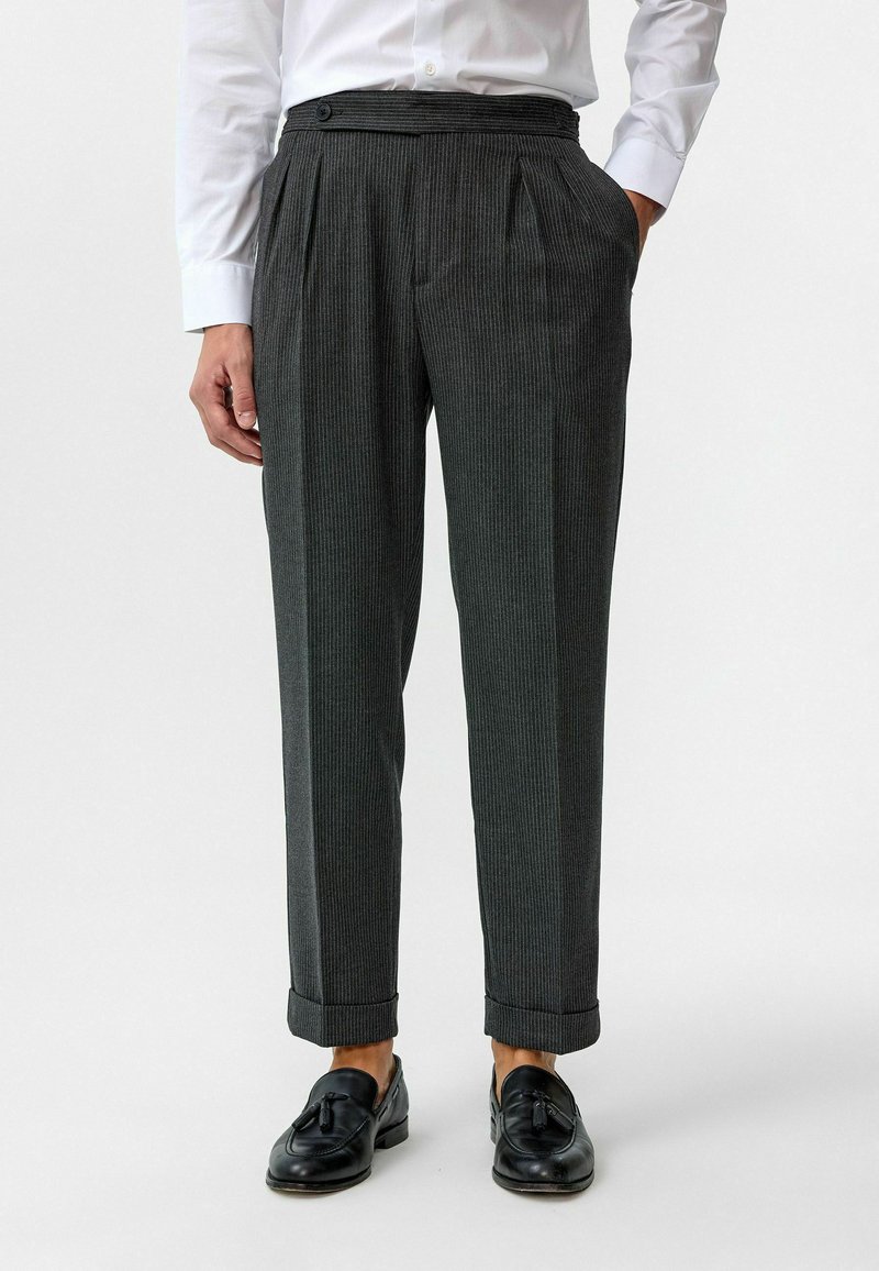 Grijze broek met streepjes, met plooien, een knoopsluiting in de taille en opgerolde boorden. Gemaakt van een textuurstof. Gecombineerd met zwarte loafers.