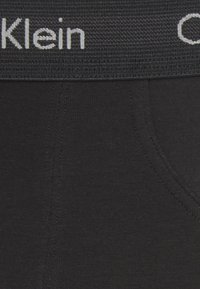 Schwarze Baumwollslips mit einem strukturierten Bund, auf dem das Logo "Calvin Klein" in Weiß abgebildet ist. Insgesamt glatte Textur mit verstärkten Nähdetails.