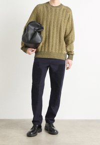 Gruby, dzianinowy sweter w oliwkowym zielonym kolorze, granatowe spodnie z teksturowanymi naszywkami oraz czarne skórzane buty, trzymające elegancką czarną torbę w stylu piankowym.