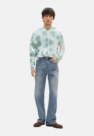 Sudadera con capucha en un patrón de tie-dye teal claro, combinada con jeans de mezclilla azul claro y zapatos marrones. Cuenta con cremallera y bolsillos frontales.
