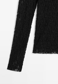 Schwarzes Spitzenoberteil mit langen Ärmeln und strukturiertem Muster, mit rundem Ausschnitt und figurbetonter Silhouette. Leichter und halbtransparenter Stoff.