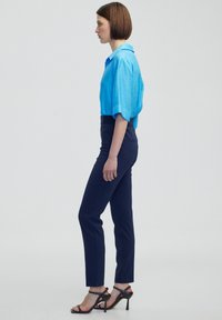 Světlé modré oversized tričko v kombinaci s přiléhavými námořnickými kalhotami. Tričko má krátké rukávy a límeček; kalhoty mají elegantní design a nenápadné kapsy.