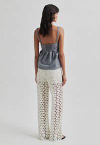 Top in satin grigio con spalline regolabili e retro arricciato, abbinato a pantaloni in crochet bianco a maglia aperta con motivi floreali.
