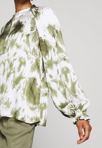 Langærmet bluse i hvid med grønt tie-dye mønster. Har en rund halsudskæring og elastiske manchetter, lavet af letvægtsstof.