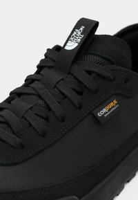 Black sneaker featuring a textured Cordura upper, reinforced toe, flat laces, and a pull tab with white branding on the tongue.