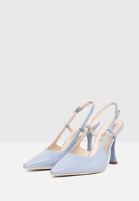 Talons slingback en cuir verni bleu clair avec des bouts pointus, dotés d'une bride ajustable et d'un talon conique modéré. Fini lisse.