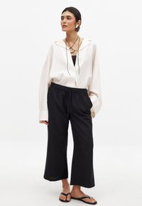 Losse witte blouse met een kraag, zwarte elastische broek en zwarte slippers. De blouse heeft subtiele naaddetails en lange mouwen.