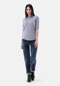 Hellgraues, kurzärmliges Oberteil mit Rundhalsausschnitt; kombiniert mit dunkelblauen, schnittigen Jeans mit umgeschlagenen Säumen und schwarzen Knöchelschuhen.