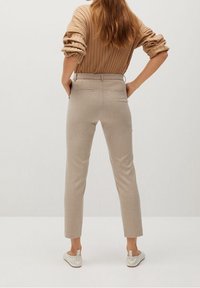Pantalon beige ajusté à coupe slim, confectionné en tissu texturé. Dispose de poches arrière et d'un design épuré et minimaliste. Porté avec un haut côtelé.