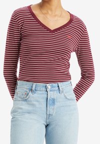 Maroon striped long-sleeve v-neck shirt with cream lines, featuring a small logo detail. Worn with high-waisted light blue jeans.