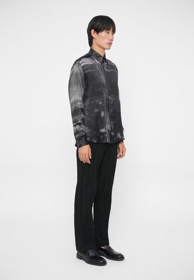 Zwarte en grijze abstracte patroon blouse met een knoopsluiting aan de voorkant, gecombineerd met gestructureerde zwarte broeken en gepolijste zwarte schoenen.