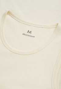 Top senza maniche a coste di colore crema con scollatura rotonda e etichetta del marchio "Matinique" stampata all'interno del colletto.