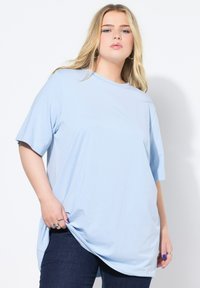 Světle modré, oversized tričko s krátkým rukávem a kulatým výstřihem, vyrobené z hladkého materiálu. V páru s tmavě modrými džíny.