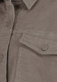 Brown corduroy shirt featuring a pointed collar, two front pockets with flaps, and round buttons. Textured fabric with vertical ribbing pattern.