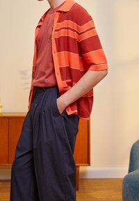 Röd-orange randig kortärmad skjorta över en enfärgad vinröd t-shirt, i kombination med lösa marinblå byxor med breda veck.