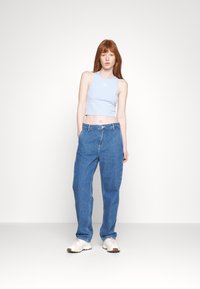Lyseblå cropped tank top med en liten logo, kombinert med løstsittende blå denimjeans og lysebeige sneakers. Nøytral bakgrunn.