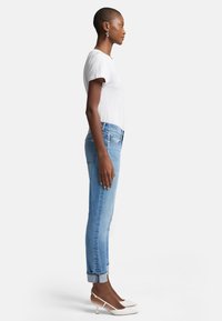 Ljusblå denimjeans med slim fit och uppvikta fållar, i kombination med en vit t-shirt med kort ärm och vita klackar. Särskilt mjuk textur.