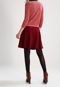 Stickad rosetröja med trekvartslånga ärmar och rund halsringning, ihopparad med en bourgognefärgad utsvängd kjol. Bruna ankelboots fulländar outfiten.