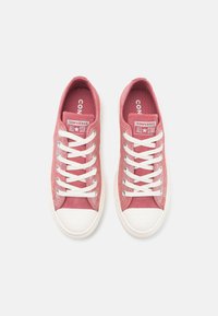 Baskets en toile roses avec des lacets blancs et des embouts en caoutchouc. Présente des marques "Converse All Star" sur la languette et sur le côté.