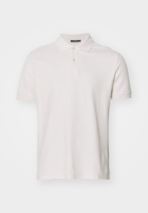 Polo shirt de color beige claro, de mangas cortas, hecho de algodón. Presenta un cierre de botones y un pequeño logo de la marca en el pecho. Textura suave.