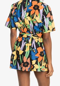 Blommig jumpsuit i bomull med korta, vida ärmar. Har en figurnära midja och livfulla mönster i orange, blått, gult och grönt på en svart bakgrund.