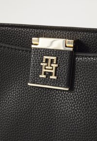 Black leather handbag with textured surface, featuring a gold clasp and a logo plaque with the initials 'TH'.
