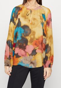 Blouse multicolore avec un motif floral bleu, rose, orange et marron, dotée d'un col rond et d'un détail noué à l'avant.