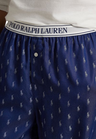 Blå mönstrade kalsonger med en vit elastisk midjeband som har texten "POLO RALPH LAUREN". Subtilt upprepat logotypmönster i grått. Knapppunkt synlig.
