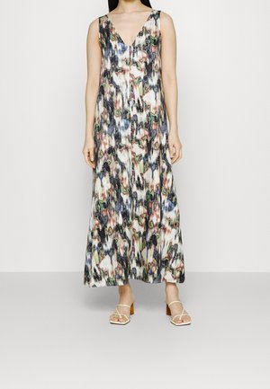 Femme portant une robe longue sans manches avec un motif abstrait multicolore et des chaussures blanches ouvertes à talon bloc.
