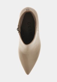Botín de cuero beige hasta el tobillo con punta afilada, cierre de cremallera lateral y interior texturizado con el nombre de la marca "GUESS."