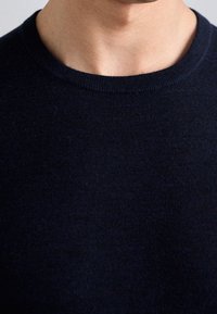 Marinblå tröja med rundad hals i mjukt material. Har en ribbad krage och en kroppsnära passform. Tyget känns mjukt och fint stickat.